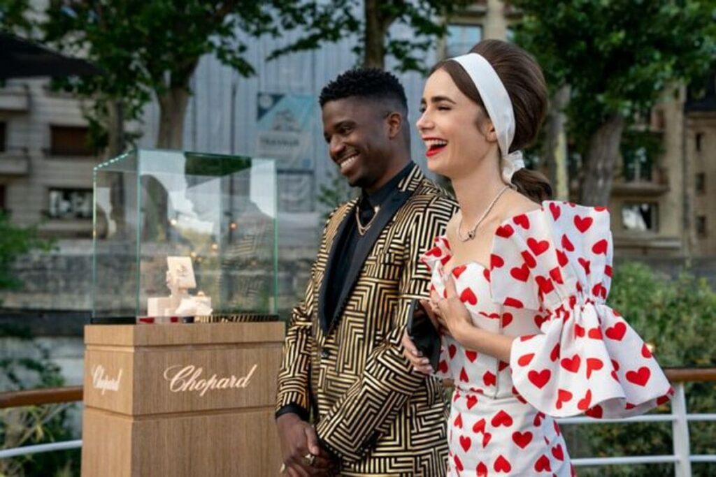 Personagens da série Emily in Paris, exibida na Netflix, sorrindo durante um evento de moda com roupas elegantes.